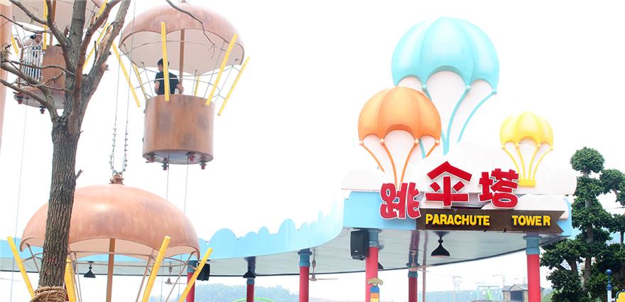 Entrance to a “Parachute Tower” amusement ride with colorful parachute decorations and hanging gondolas.