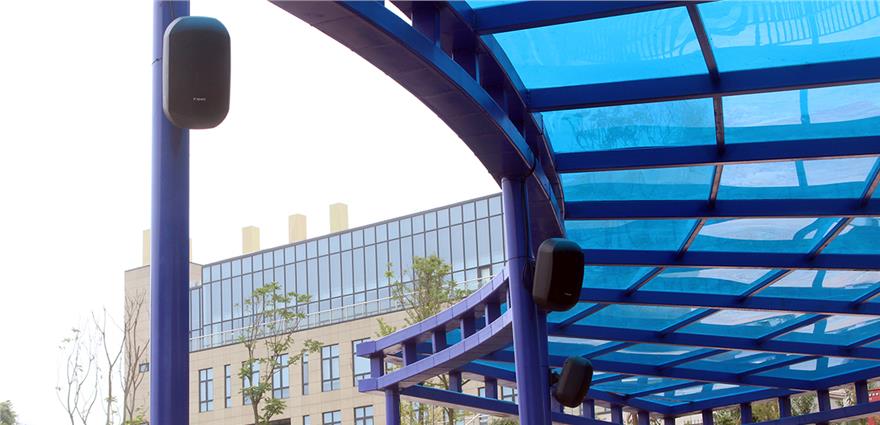 Blue steel canopy structure at an amusement park with black speakers mounted on the support columns.