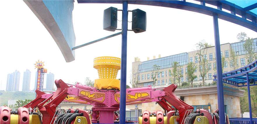 Colorful spinning amusement ride with pink arms and yellow hub beneath a blue canopy and mounted speakers.