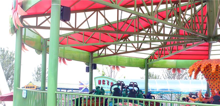 Covered amusement park ride with green framework, red canopy, and rows of suspended seats.