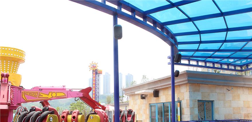 Amusement park ride with pink seats under a blue-tinted canopy and nearby stone building.