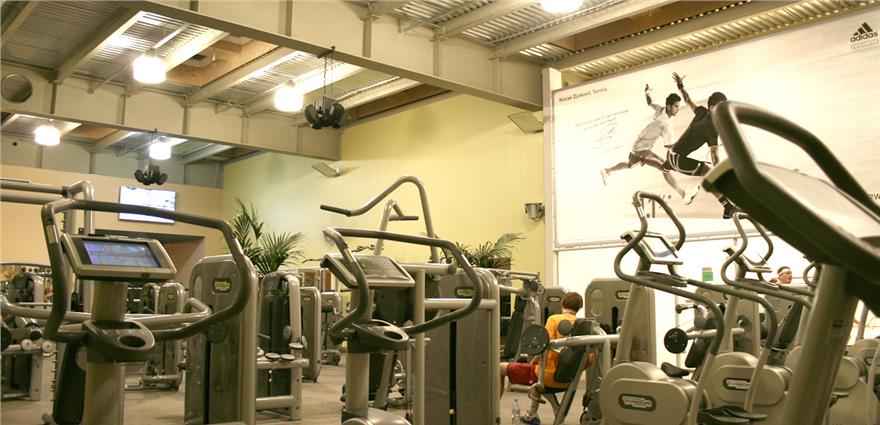 Gym room filled with strength machines and cardio equipment under high industrial-style ceilings.