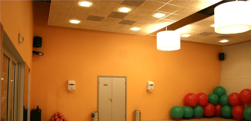 Fitness studio with orange walls, exercise balls stacked in the corner, and pendant lights from a tiled ceiling.