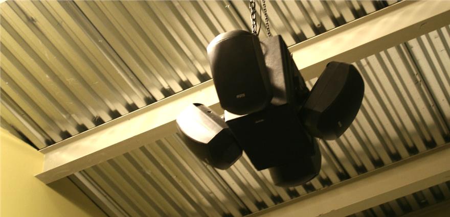 Cluster of black loudspeakers suspended from a corrugated metal ceiling.