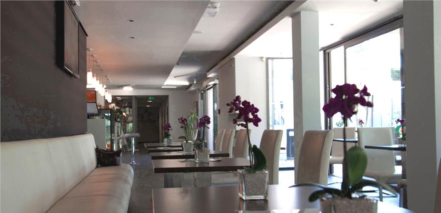 Modern café or lounge with white seating, tables lined with potted orchids, and large windows.