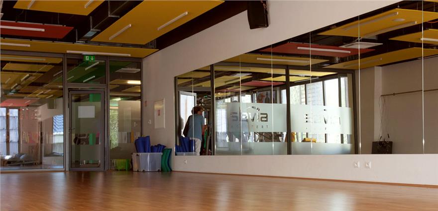 Spacious fitness or dance studio with mirrored wall, wooden floor, and colorful ceiling panels.