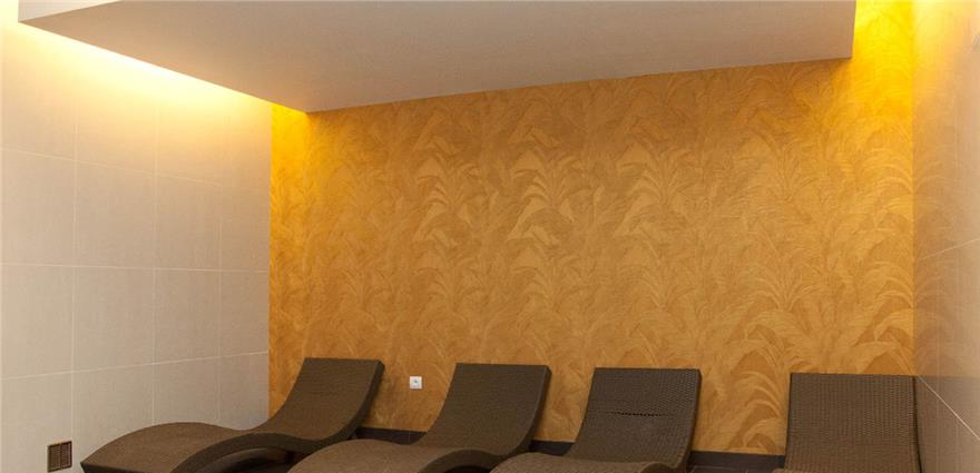 Spa relaxation room with wicker lounge chairs against a warm yellow textured wall and soft ceiling lighting.