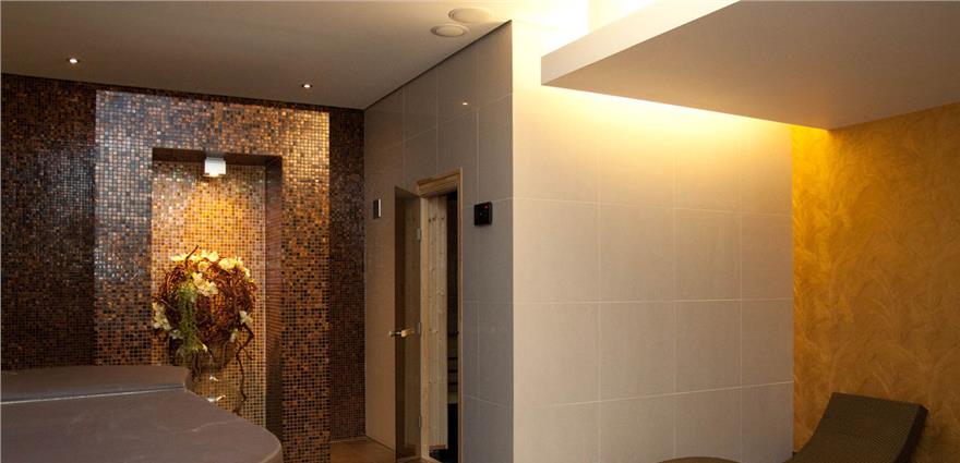 Spa relaxation room with mosaic-tiled wall niche, warm lighting, and lounge chairs.