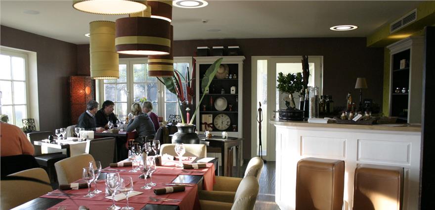 Cozy restaurant interior with set tables, hanging drum lamps, and a small bar counter.