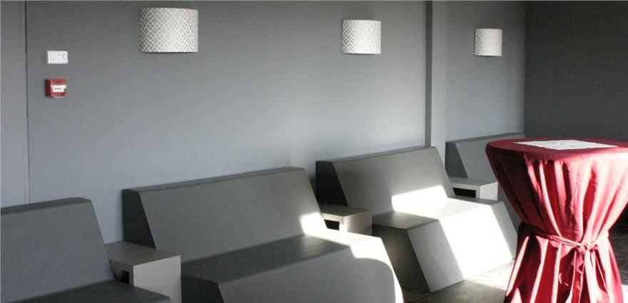 Minimalist gray lounge with angular bench seating and a tall cocktail table draped in red cloth.