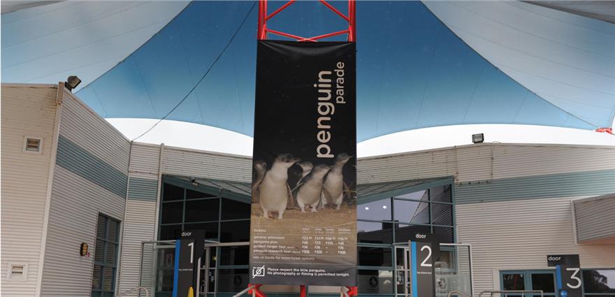 Entrance area with large “Penguin Parade” banner showing penguins, beneath a curved canopy roof.