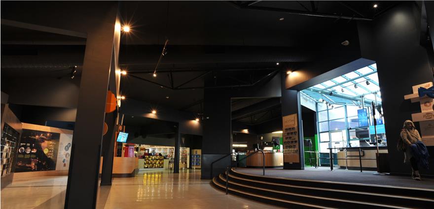 Spacious, dimly lit museum or aquarium lobby with exhibits, gift shop, and stepped entrance area. Spacious, dimly lit museum lobby with exhibits, gift shop displays, and a stepped entrance area.