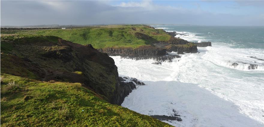 Rugged green cliffs along a rocky coastline with waves crashing against the shore.