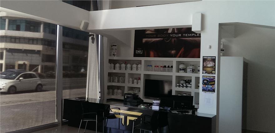 Gym reception area with supplement shelves, front desk, large windows, and poster reading “YOUR BODY YOUR TEMPLE.”