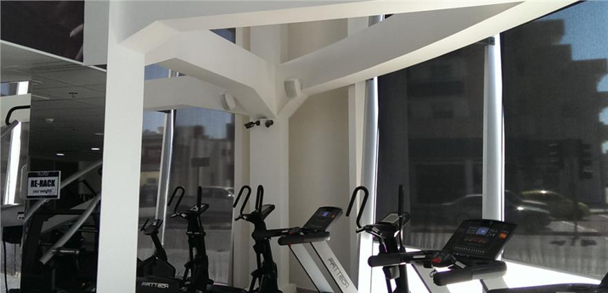 Sunlit gym corner with stationary bikes positioned near large windows and white structural beams.