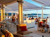 Outdoor waterfront restaurant patio with shaded seating, ambient lighting and relaxed guests