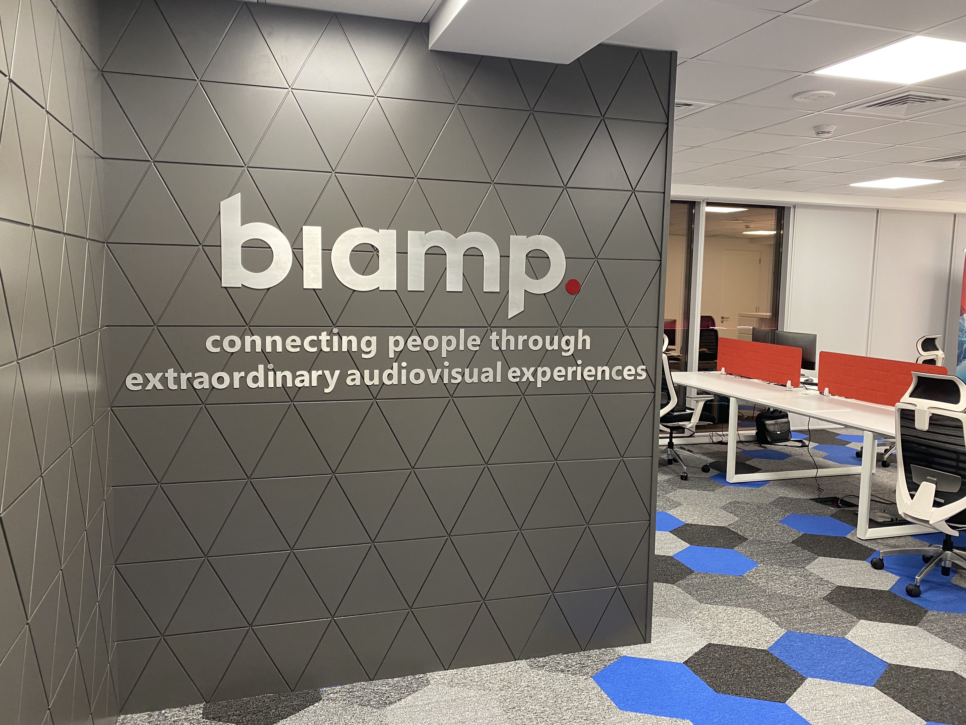 Biamp office interior with brand wall reading “connecting people through extraordinary audiovisual experiences” and open workstations