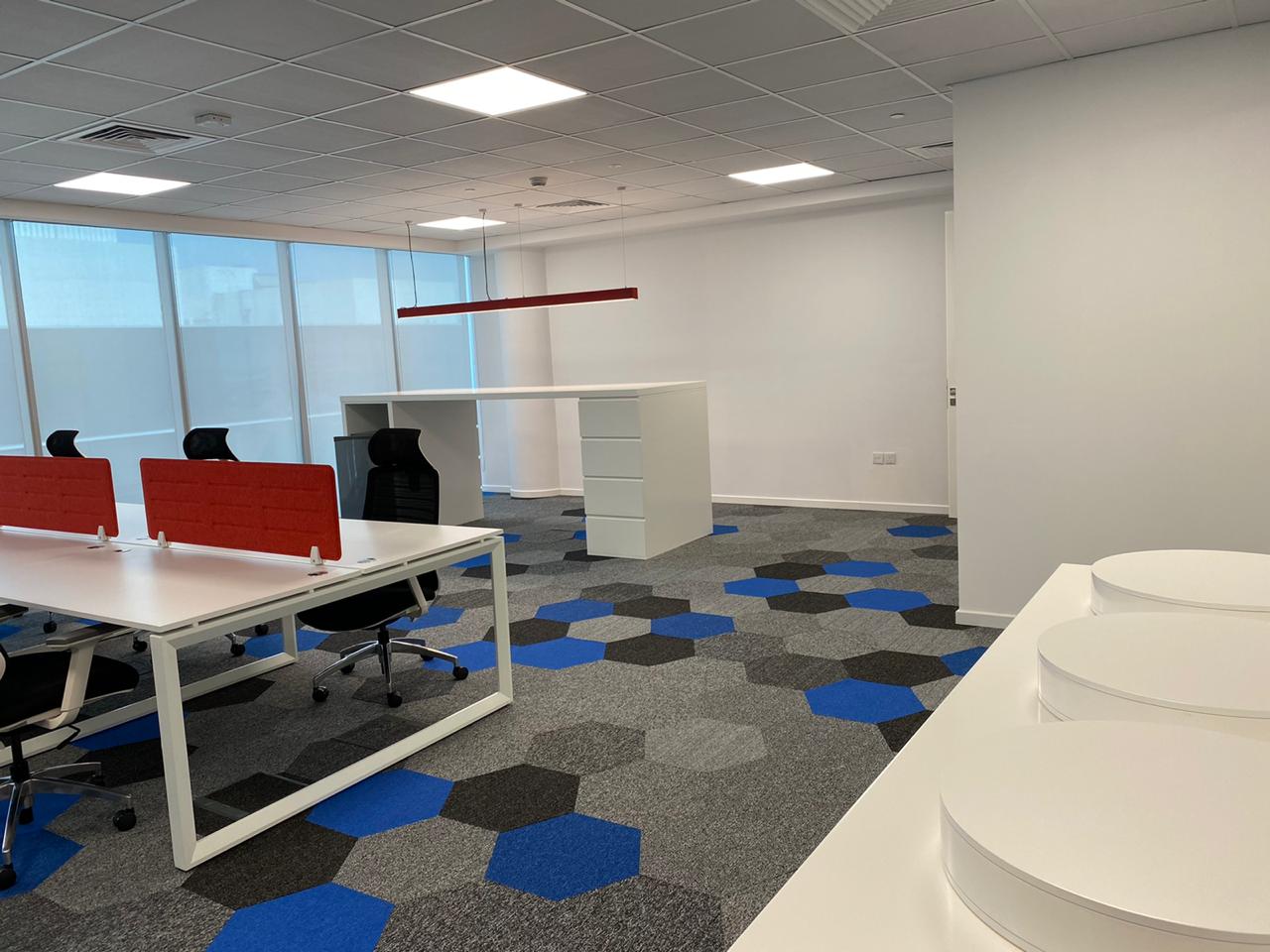 Modern open office with white desks, red privacy screens, and blue‑gray hexagon carpet tiles
