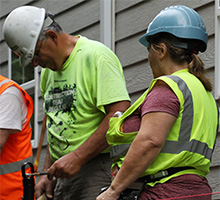 Construction workers in safety vests and hard hats collaborating on a building exterior