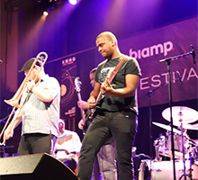 Live band performing on stage at Biamp‑sponsored music festival with guitar, trombone and drums