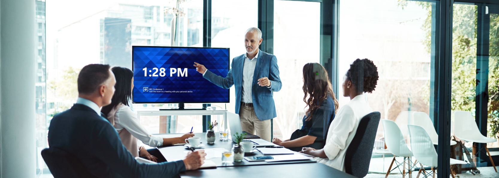 Business presentation in glass-walled conference room with digital display and team collaborating around table