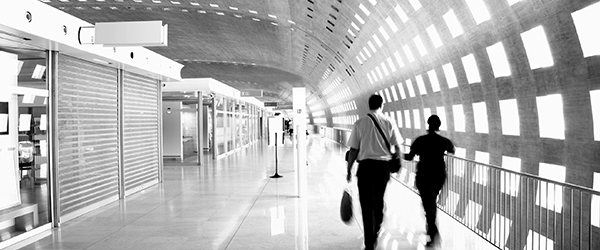Black and white modern airport or transit terminal corridor with travelers walking toward bright windows