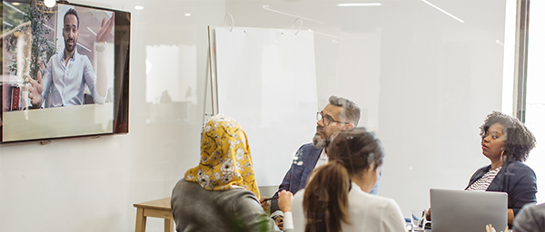 Hybrid meeting with diverse team in conference room video conferencing with remote colleague on wall display
