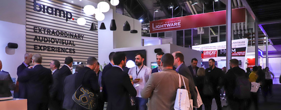 Crowd of attendees networking at the Biamp booth during a trade show, surrounded by AV company displays.