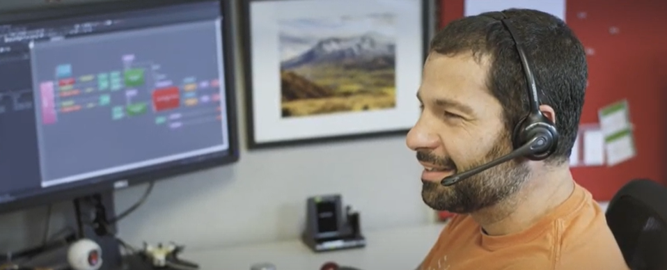 Man wearing a headset smiles while working at a computer with software open on a large monitor.
