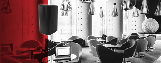 Black loudspeaker highlighted on a red overlay above a stylish, monochrome lounge with modern seating.