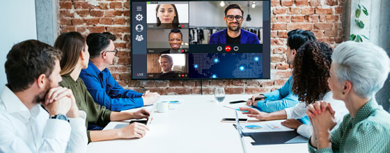 Group of colleagues in a conference room watching participants on a large screen during a video meeting.