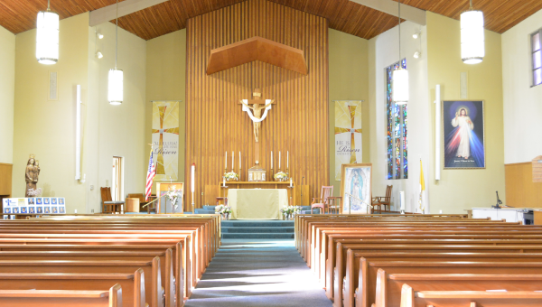 Bright church interior with wooden pews facing altar, crucifix, stained glass and religious artwork