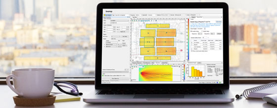 Laptop on a desk displaying Biamp acoustic design software, with city skyline blurred in the background.