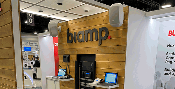 Biamp trade show booth featuring wood accent wall with Biamp logo, mounted loudspeakers, and demo stations showcasing paging and audio solutions.
