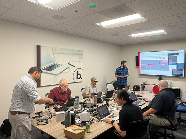 Biamp training session with participants working on laptops and AV hardware while instructor presents system configuration on large display.