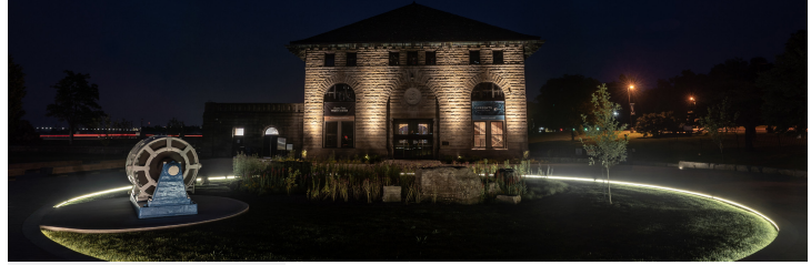 Nighttime view of a historic stone building and illuminated circular pathway, highlighting architectural lighting and outdoor sound system potential.