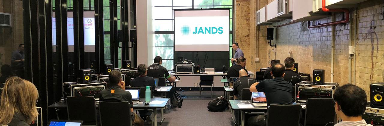 Technical training session with attendees using laptops and audio gear while an instructor presents Jands content on a projection screen.