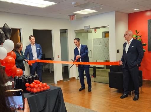 Ribbon‑cutting ceremony at a modern office, with executives in suits opening a new Biamp facility decorated with branded balloons and gifts.