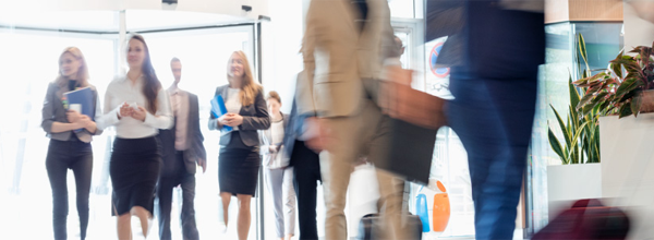 Business professionals walking through a bright corporate lobby, symbolizing a busy, modern workplace with employees on the move.