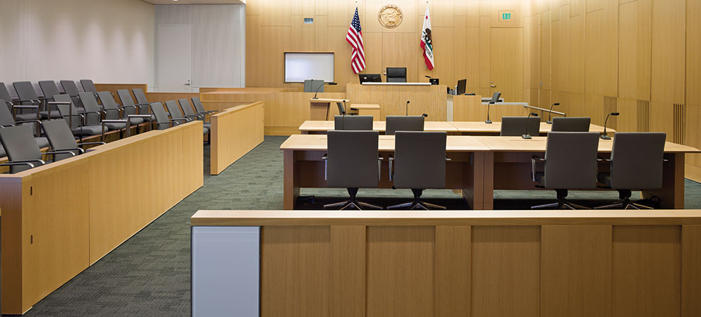 Modern courtroom interior with judge’s bench, counsel tables, jury box, and microphones, illustrating technology‑enabled judicial environment.