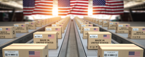 Conveyor lines of shipping boxes labeled “Made in United States” under large American flags, highlighting Biamp products manufactured in the USA.