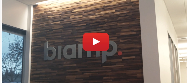 Biamp office lobby video thumbnail featuring Biamp logo on modern wood accent wall inside corporate headquarters.