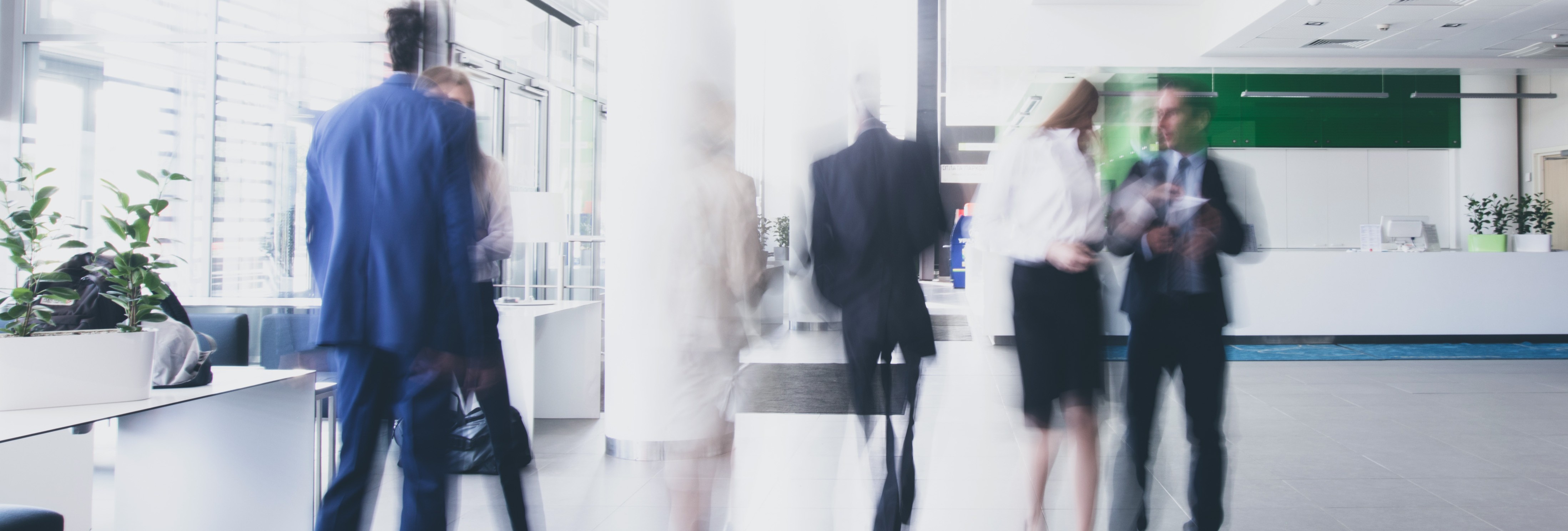 Blurred motion shot of business professionals walking through a bright modern office lobby.