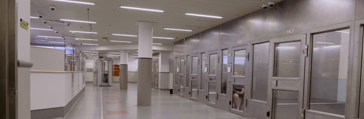 Modern detention center corridor with secure holding cells and surveillance cameras, illustrating safe, monitored inmate housing design.