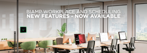 Modern open-plan office with desks, computers and a room scheduling touch panel, overlaid text: “Biamp Workplace and Scheduling – New Features Now Available.”