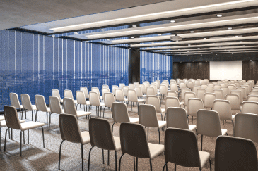Large presentation room with rows of chairs facing a projection screen and floor-to-ceiling windows.